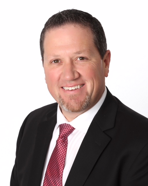 Mark Vos Man seated and smiling at the camera in a suit
