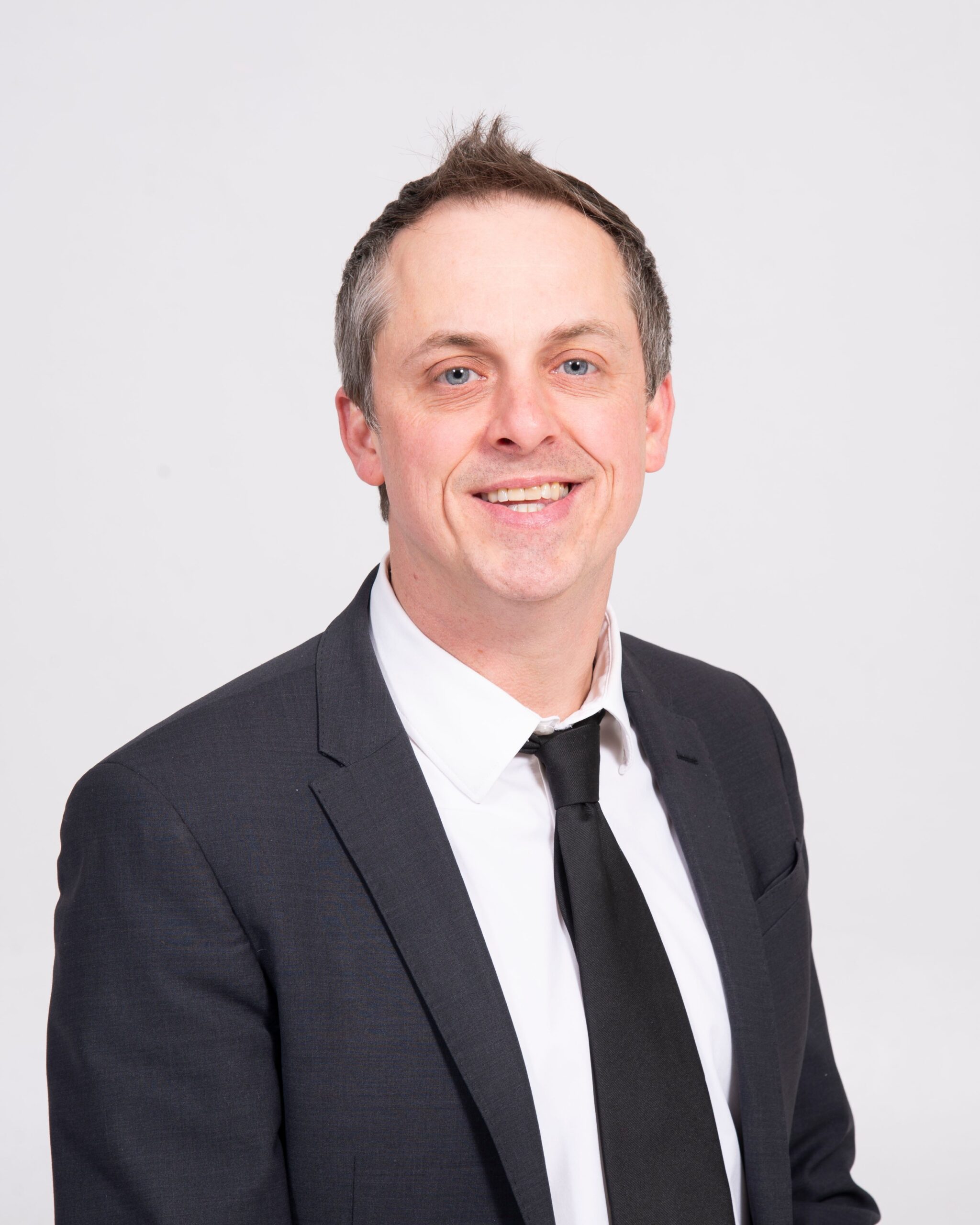 Man in black suit jacket and tie smiling